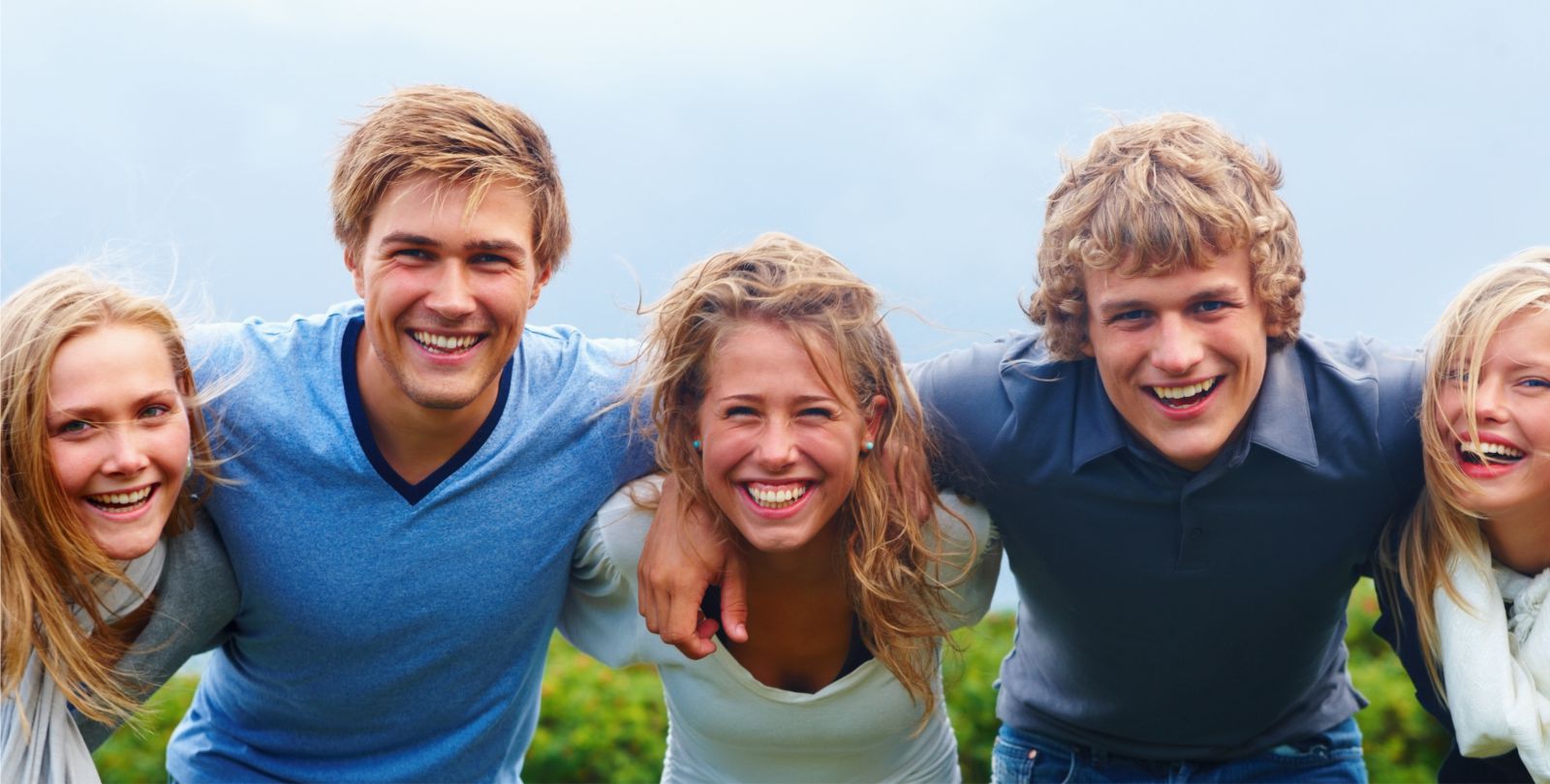 Fnf junge Erwachsene lachen Arm in Arm in die Kamera