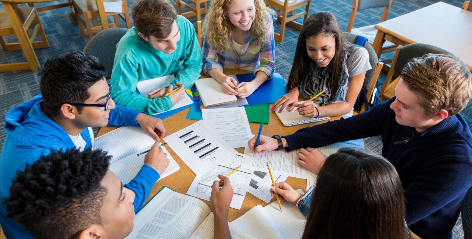 Eine Gruppe junger Menschen sitzt an einem runden Tisch und lernt gemeinsam