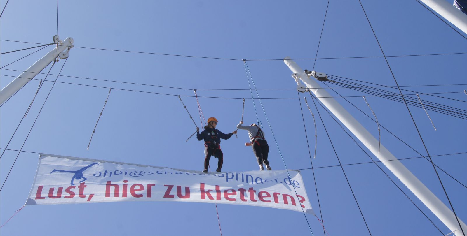 Zwei Kletterer klettern gesichert in der Takelage der Cap San Diego - Darunter ein groes Banner Lust, hier zu klettern?!