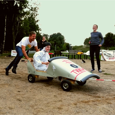 Team-Event Seifenkistenrennen Seifenkistenrennen - ein schiebt eine Frau mit ihrer Seifenkiste an