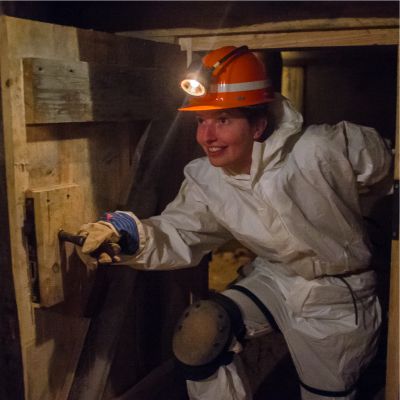 Junge Frau mit Helm in Bergwerksausrstung erkundet einen Bergwerksstollen