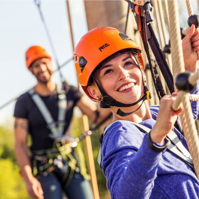 Junge Frau mit Helm klettert in einem Kletternetz