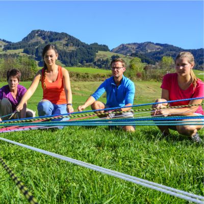 Team-Event Team-Olympiade Teamspiel - eine Gruppe versucht gemeinsam Bälle mit Schnüren zu einem Mittelpunkt zu lenken