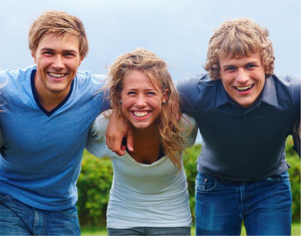 Drei Jugendliche lachen Arm in Arm in die Kamera